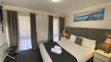 Een hotelkamer met een groot bed, twee nachtkastjes met lampen, een schilderij aan de muur en een raam met gordijnen.