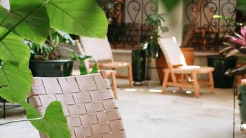 A wicker chair with a woven backrest and seat, positioned in an outdoor patio area with potted plants and a wrought iron fence in the background.