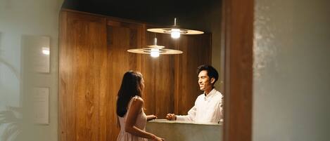 A woman in a white dress standing at a reception desk in a room with wooden walls and a tiled floor.