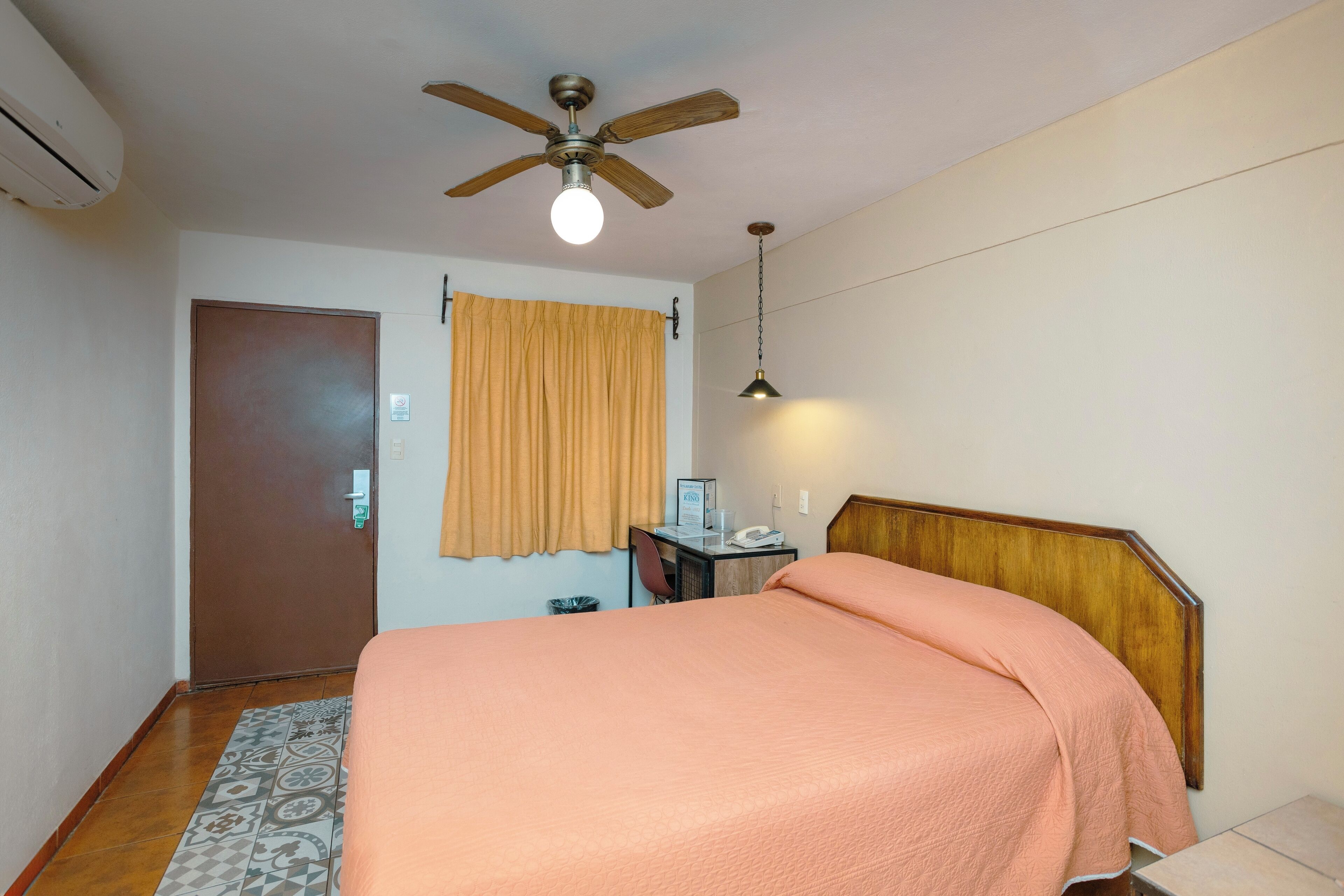 Una camera da letto con un letto, una scrivania, una sedia, una ventola a soffitto e una lampada a parete.