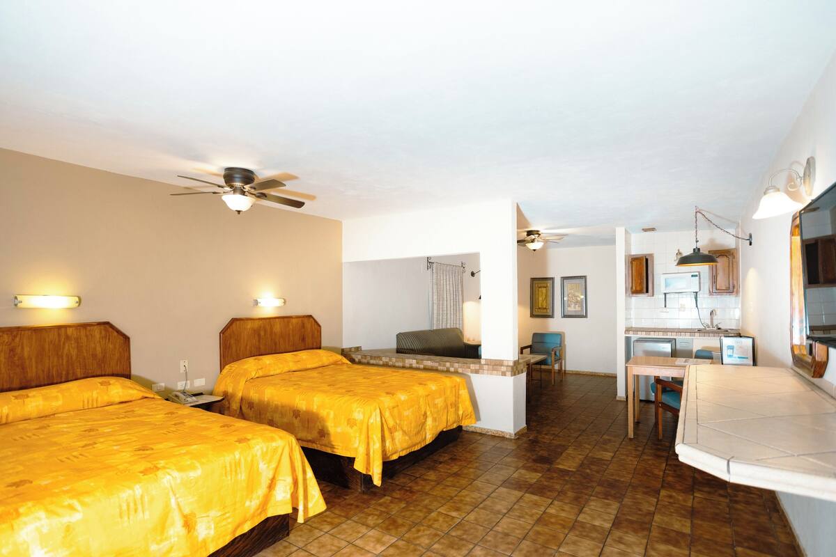 A hotel room with two beds, a kitchenette, a dining area, and a ceiling fan.