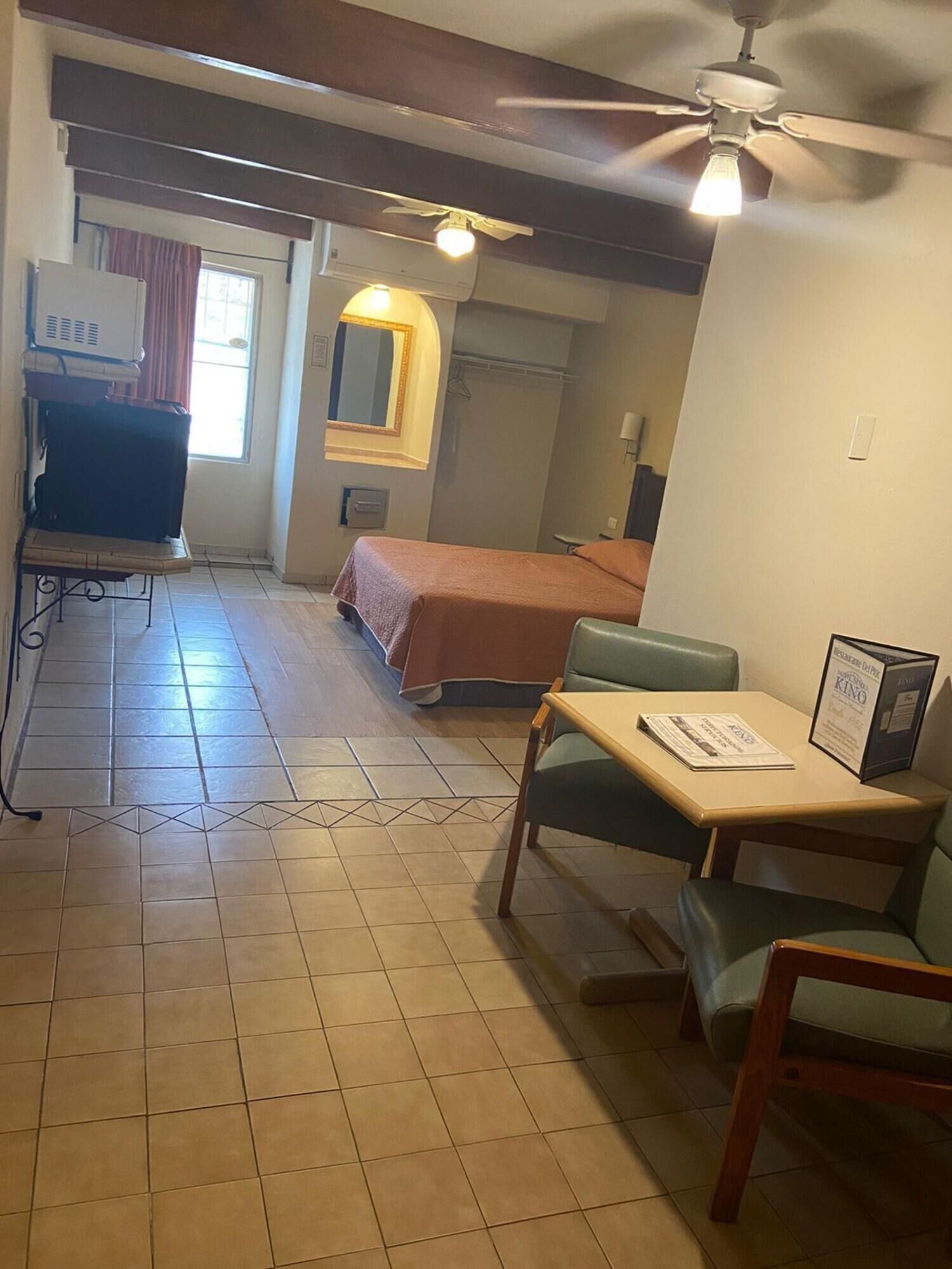 Ein Hotelzimmer mit Bett, Schreibtisch mit Stuhl, Deckenventilator, Fernseher und einem Fenster mit Vorhängen.