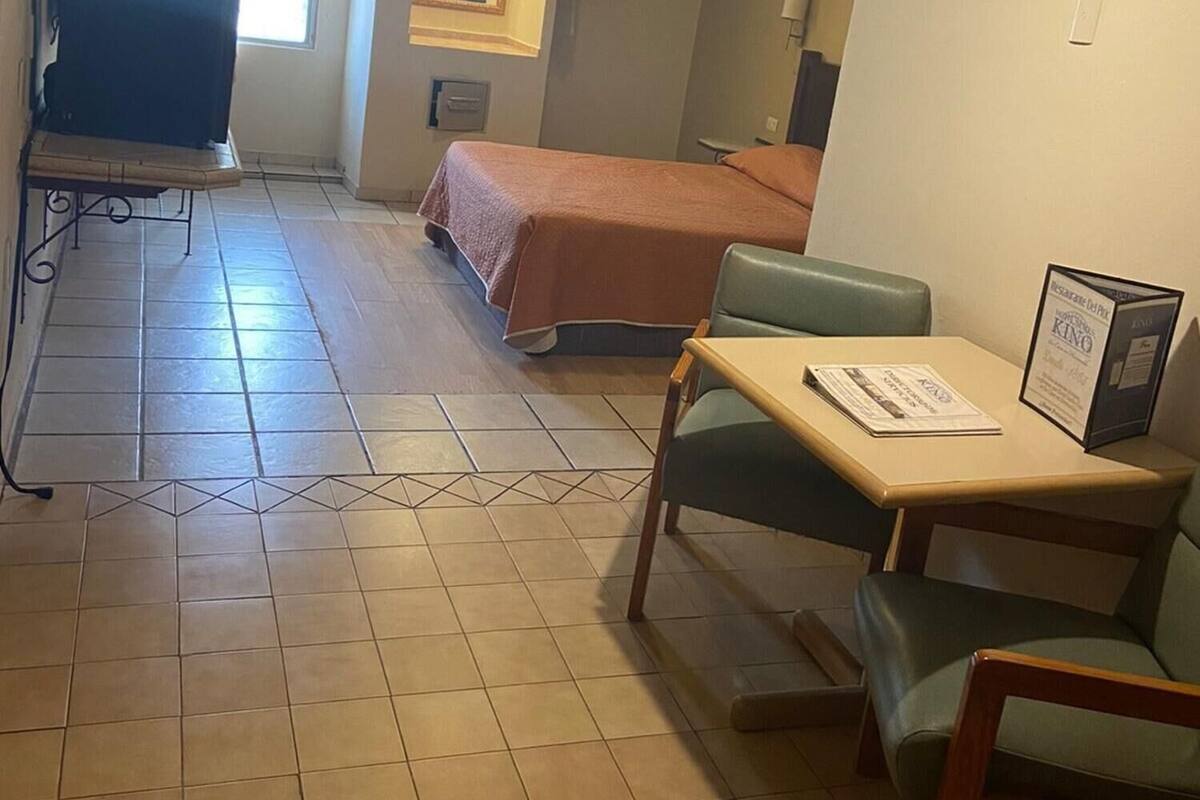 A hotel room with a bed, a desk with a chair, a ceiling fan, a TV, and a window with curtains.
