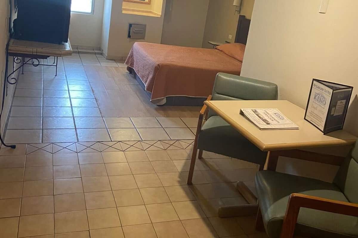 Habitación de hotel con cama, escritorio con silla, ventilador de techo, televisión y ventana con cortinas.