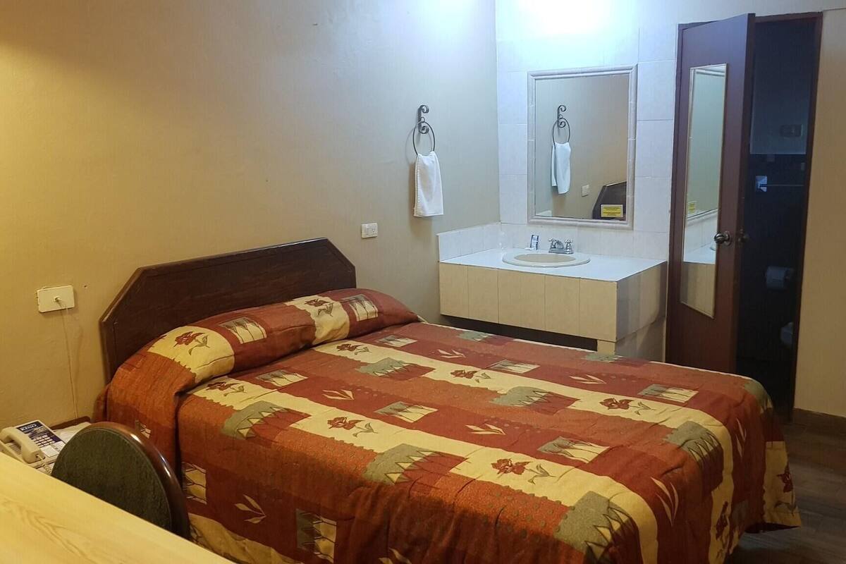 A hotel room with a bed, a bathroom with a sink and mirror, and a door.