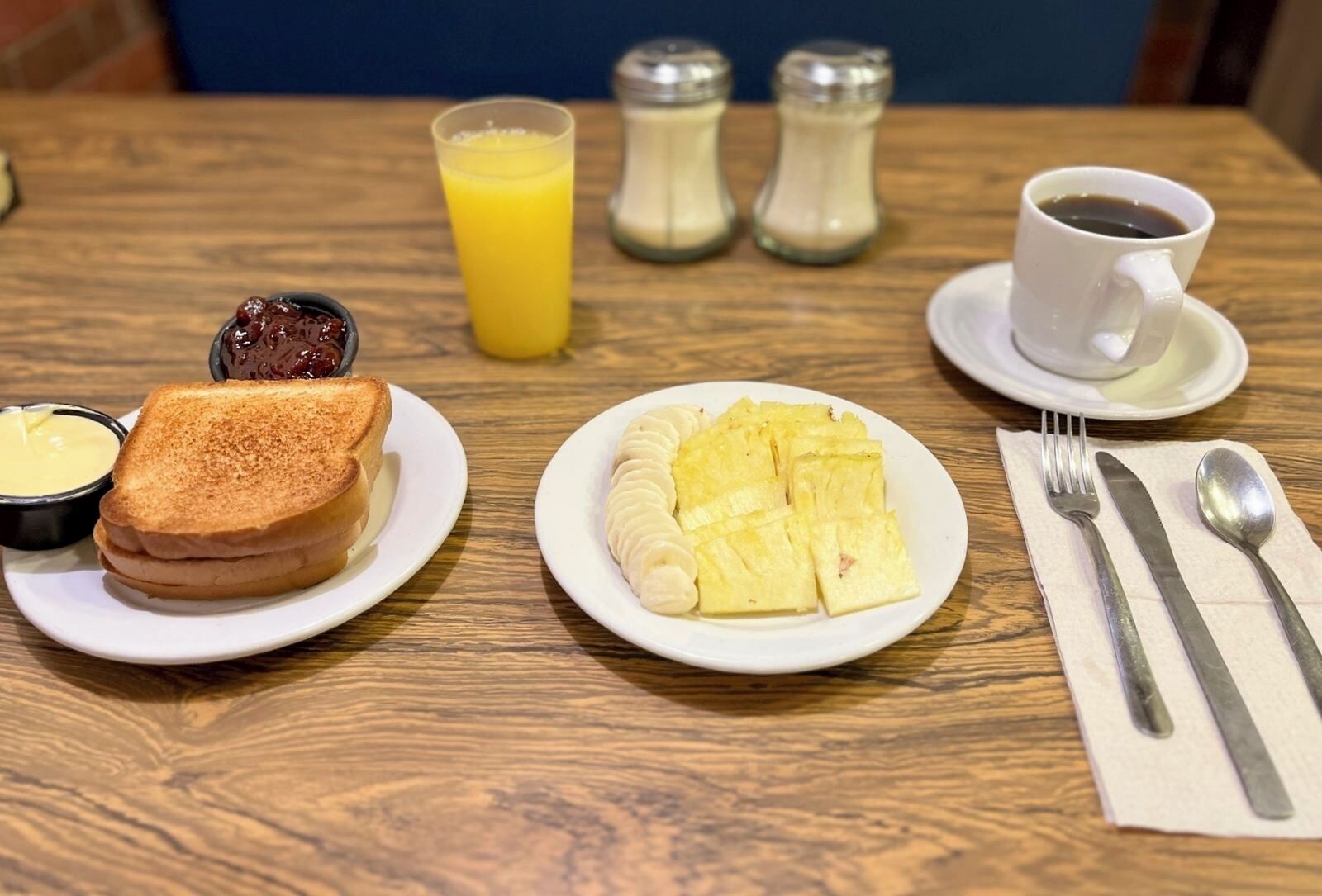 A breakfast setting with toast, scrambled eggs, a glass of orange juice, a cup of coffee, and condiments on a wooden table.