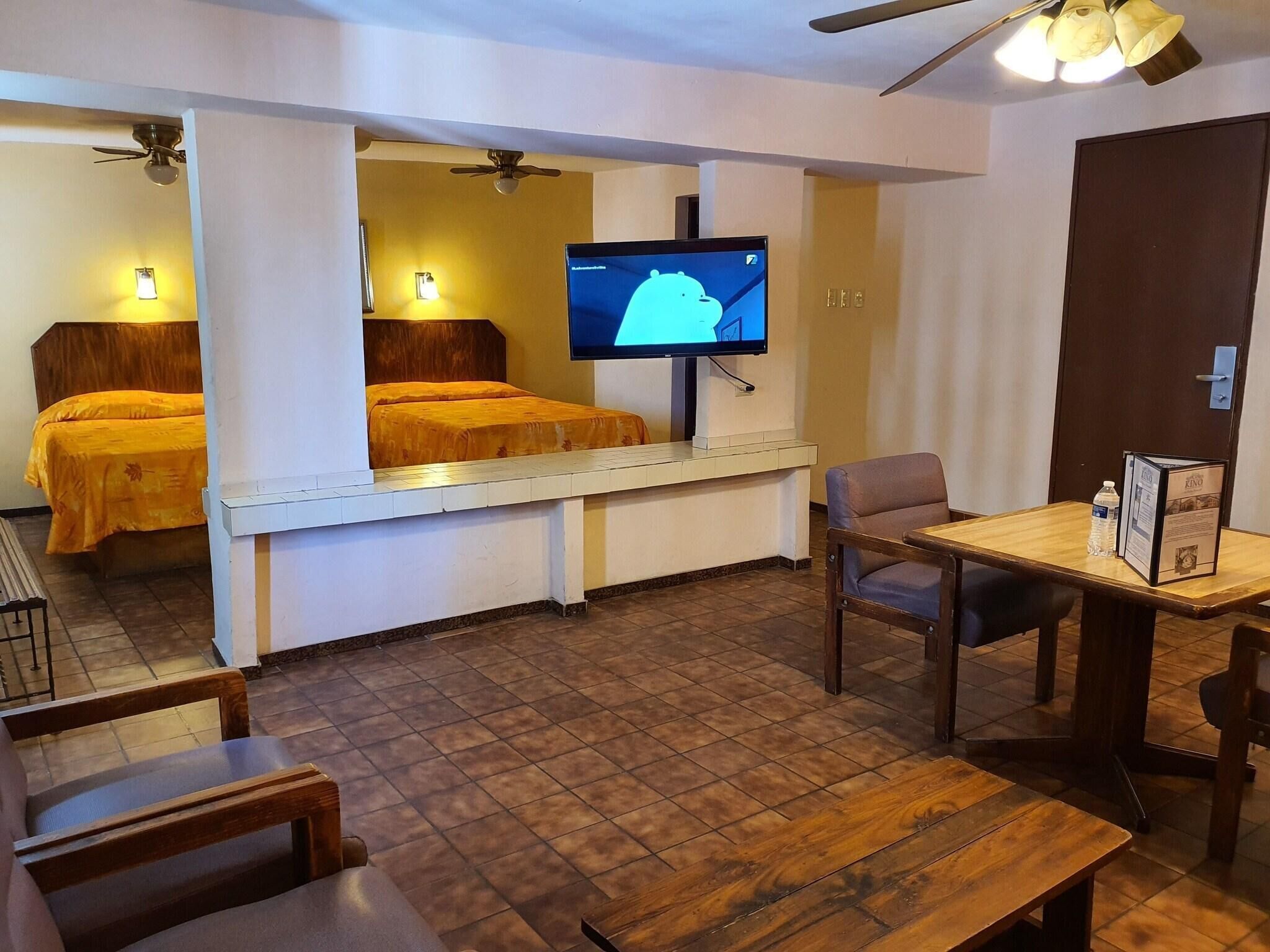 Ein Hotelzimmer mit einem Bett, einem Schreibtisch mit Stuhl, einem Fernseher und einer Wasserflasche auf dem Schreibtisch.