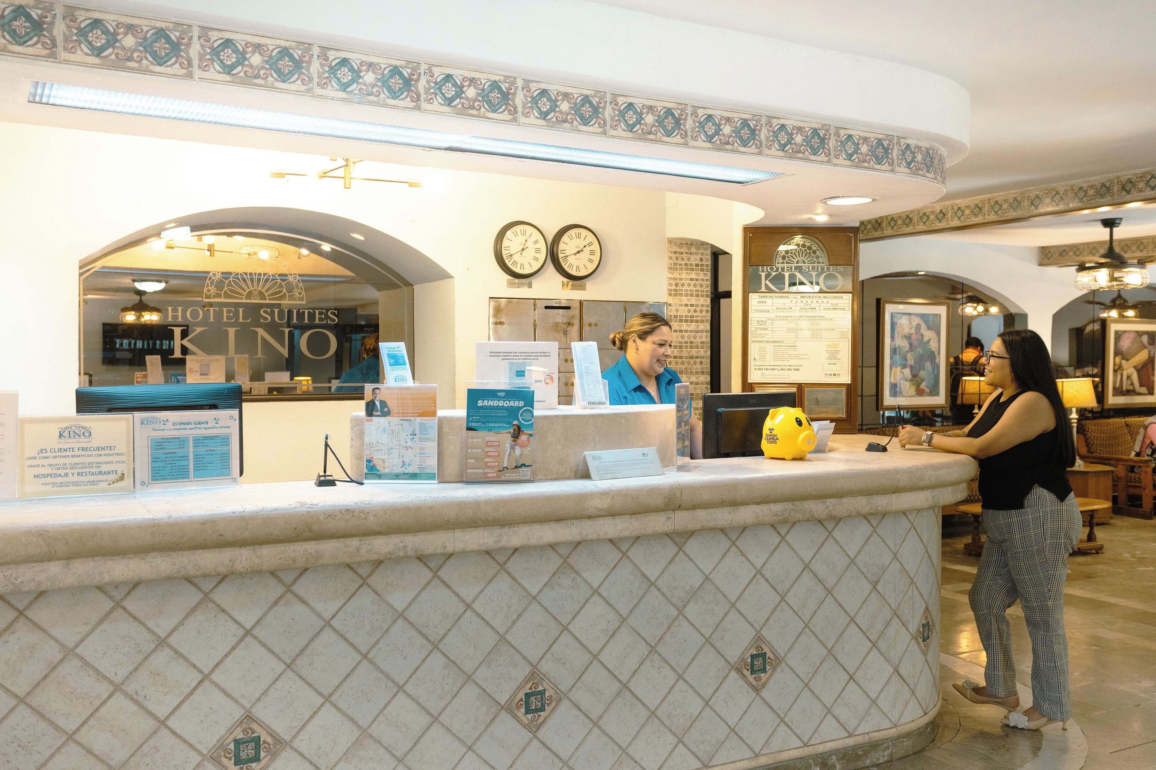 A hotel reception desk with a clock, a menu board, and a framed picture on the wall.
