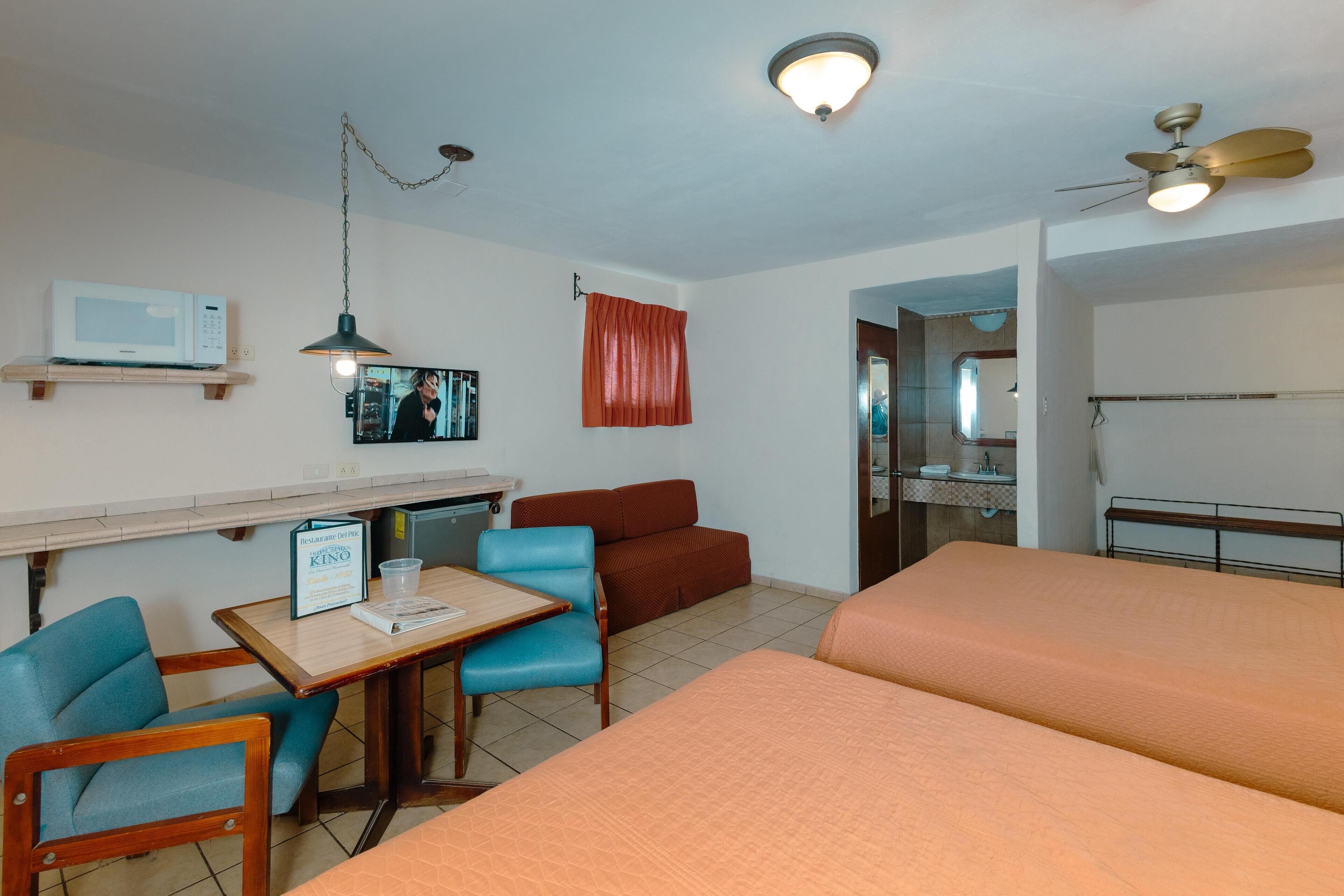 A hotel room with a kitchenette, a dining area with a table and chairs, a sofa, and a bed.