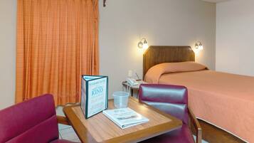 A hotel room with a bed, a desk with two chairs, a ceiling fan, and a window with curtains.