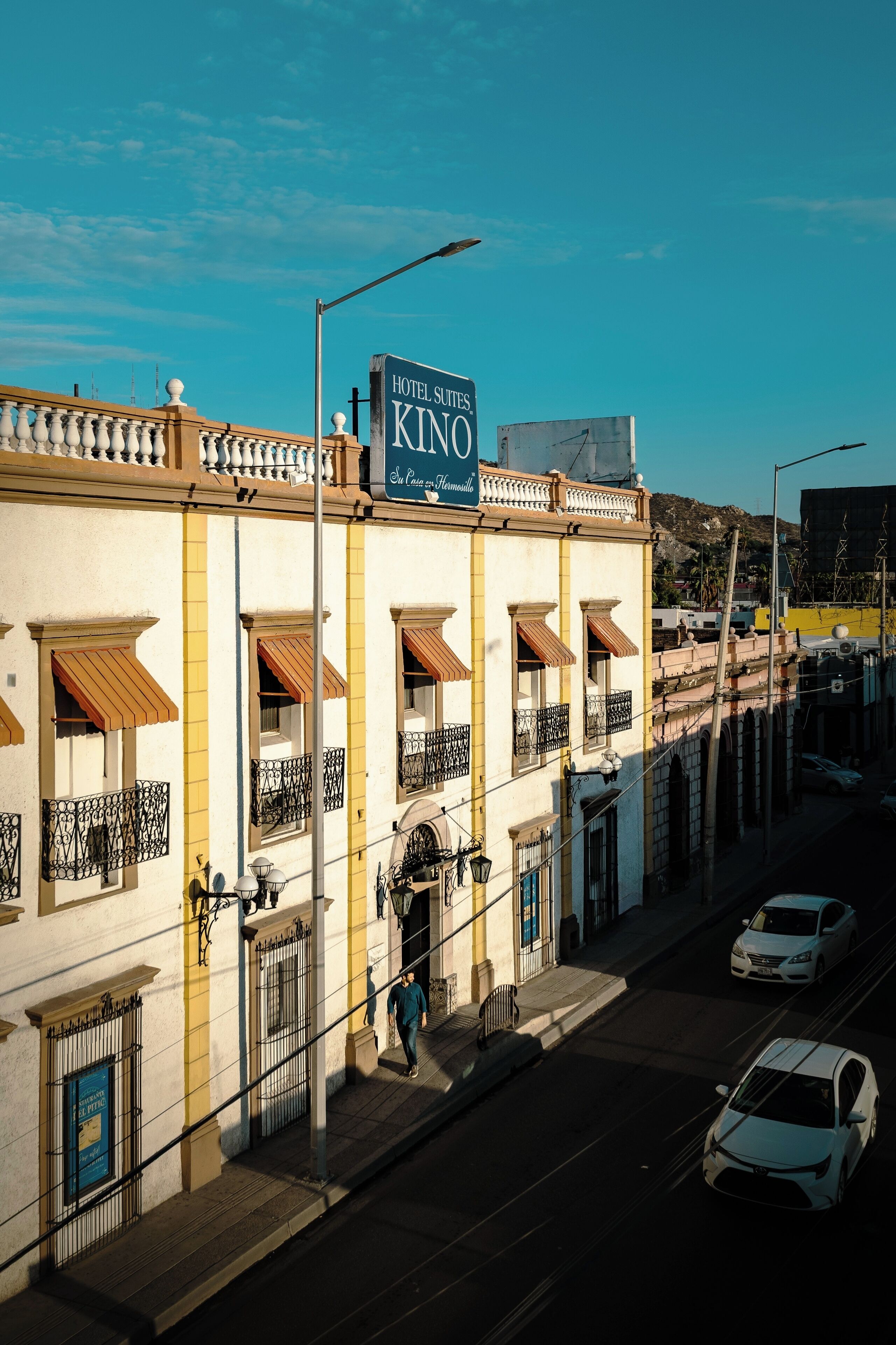 Un hotel con un cartel que dice 'HOTEL SUITES KINO' y una persona caminando por la acera.
