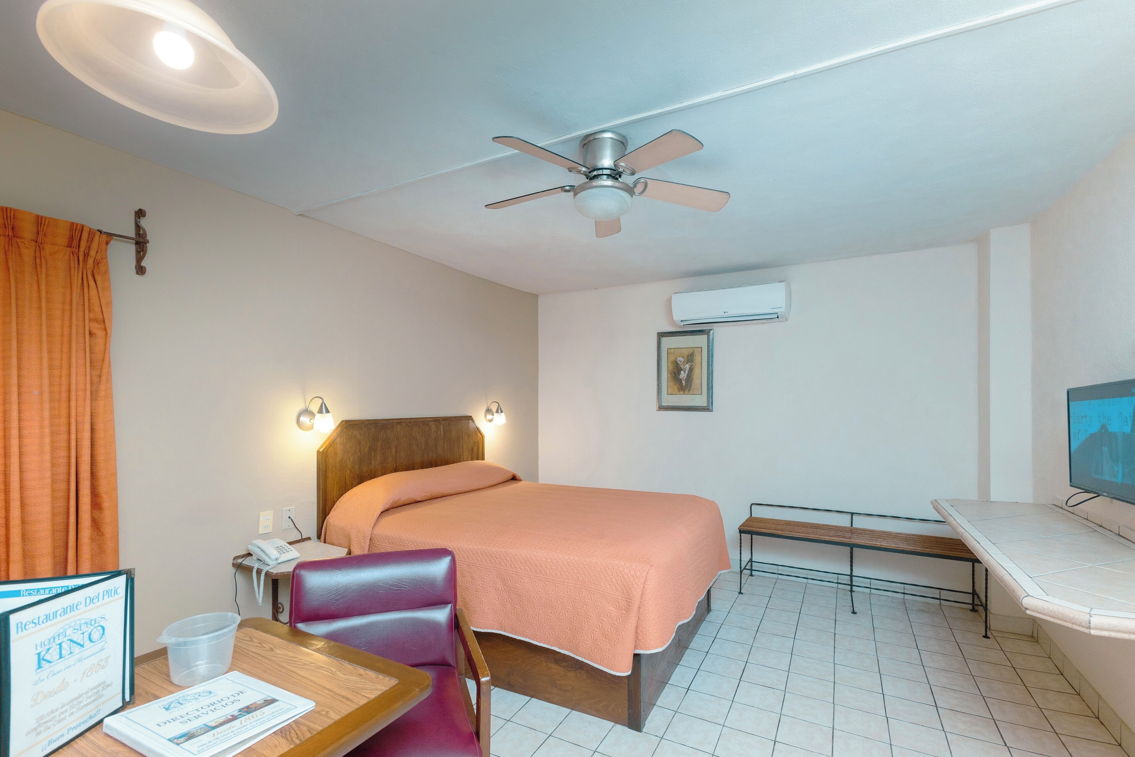 Una habitación de hotel con cama, escritorio, silla, ventilador de techo y aire acondicionado.