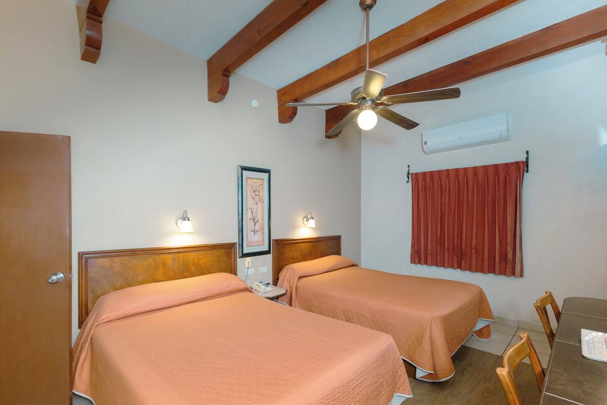 A hotel room with two beds, a ceiling fan, an air conditioning unit, a table, and chairs.