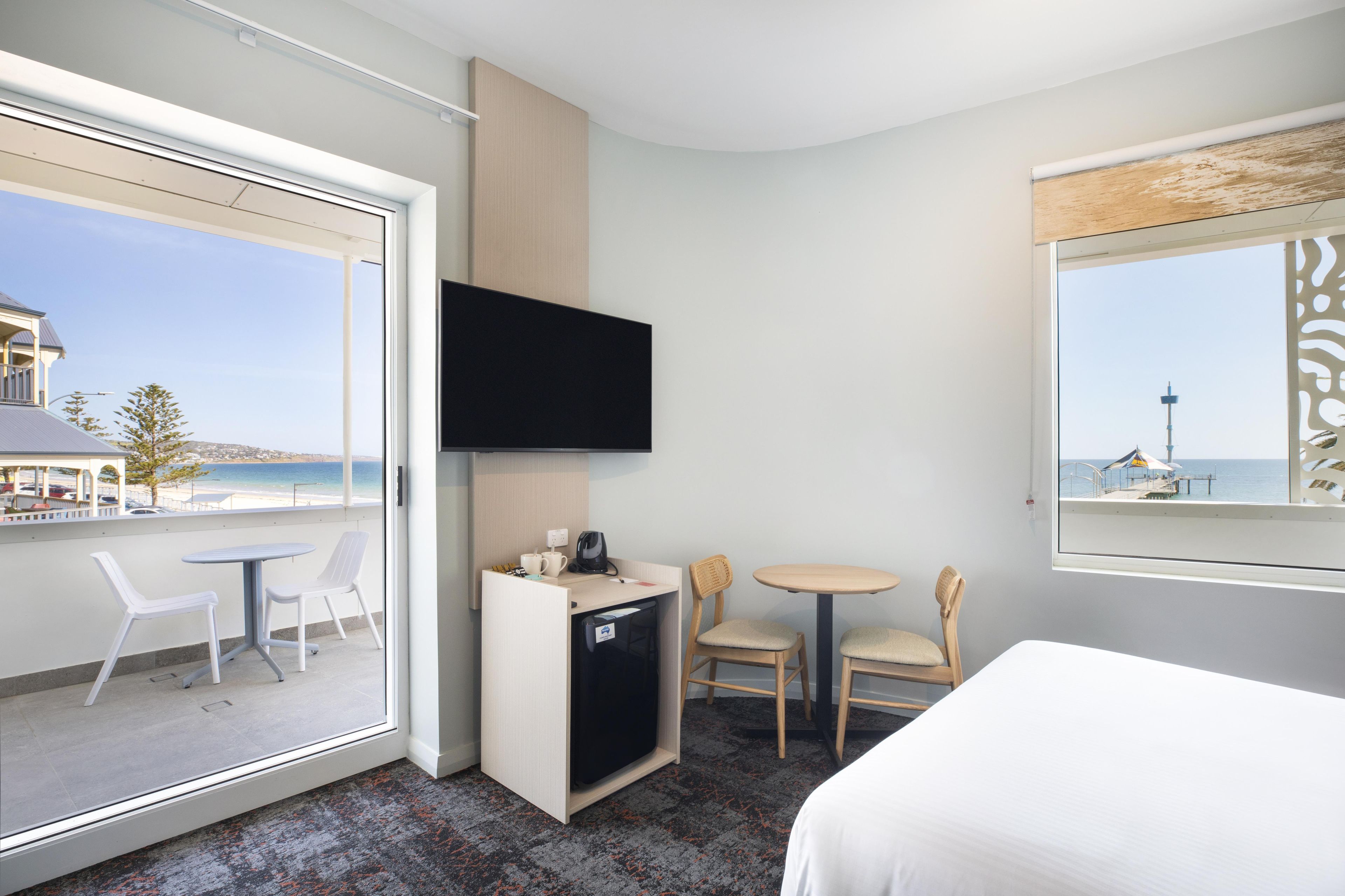A hotel room with a balcony, a TV, a desk with chairs, and a bed.