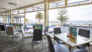 Un restaurante con amplios ventanales que ofrece vistas al mar y coches aparcados.