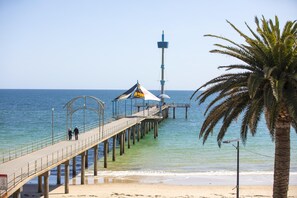 A pier extending into the sea with a lighthouse in the background, palm trees, and clear skies. - Nightcap at Esplanade Hotel (Brighton)