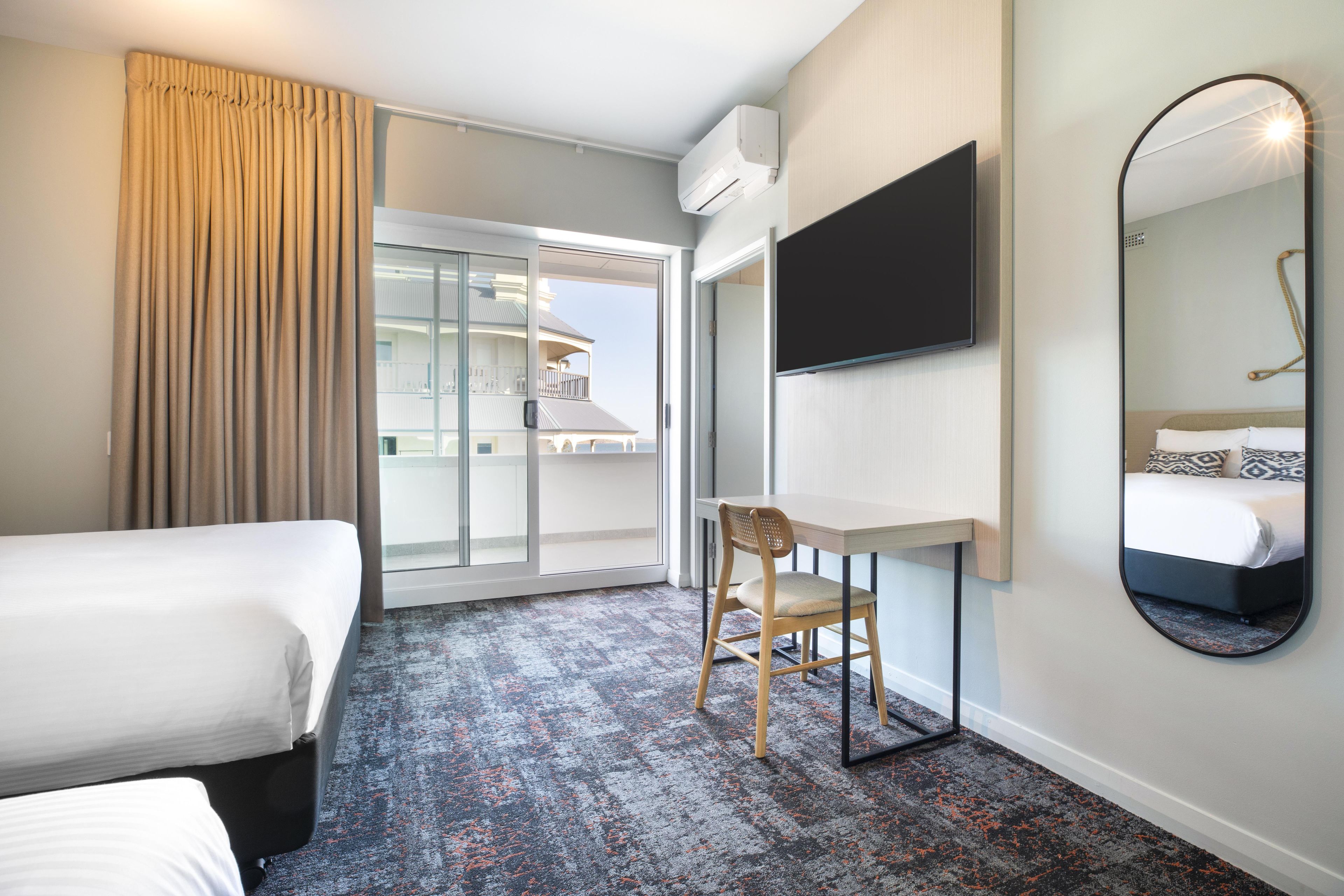 Una habitación de hotel con una cama, un escritorio, una silla, un televisor y un espejo grande.