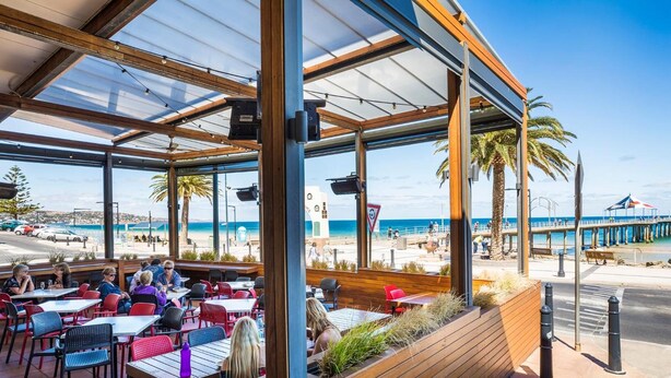 Un área de comedor al aire libre con mesas y sillas, con vista a una playa y al mar.
