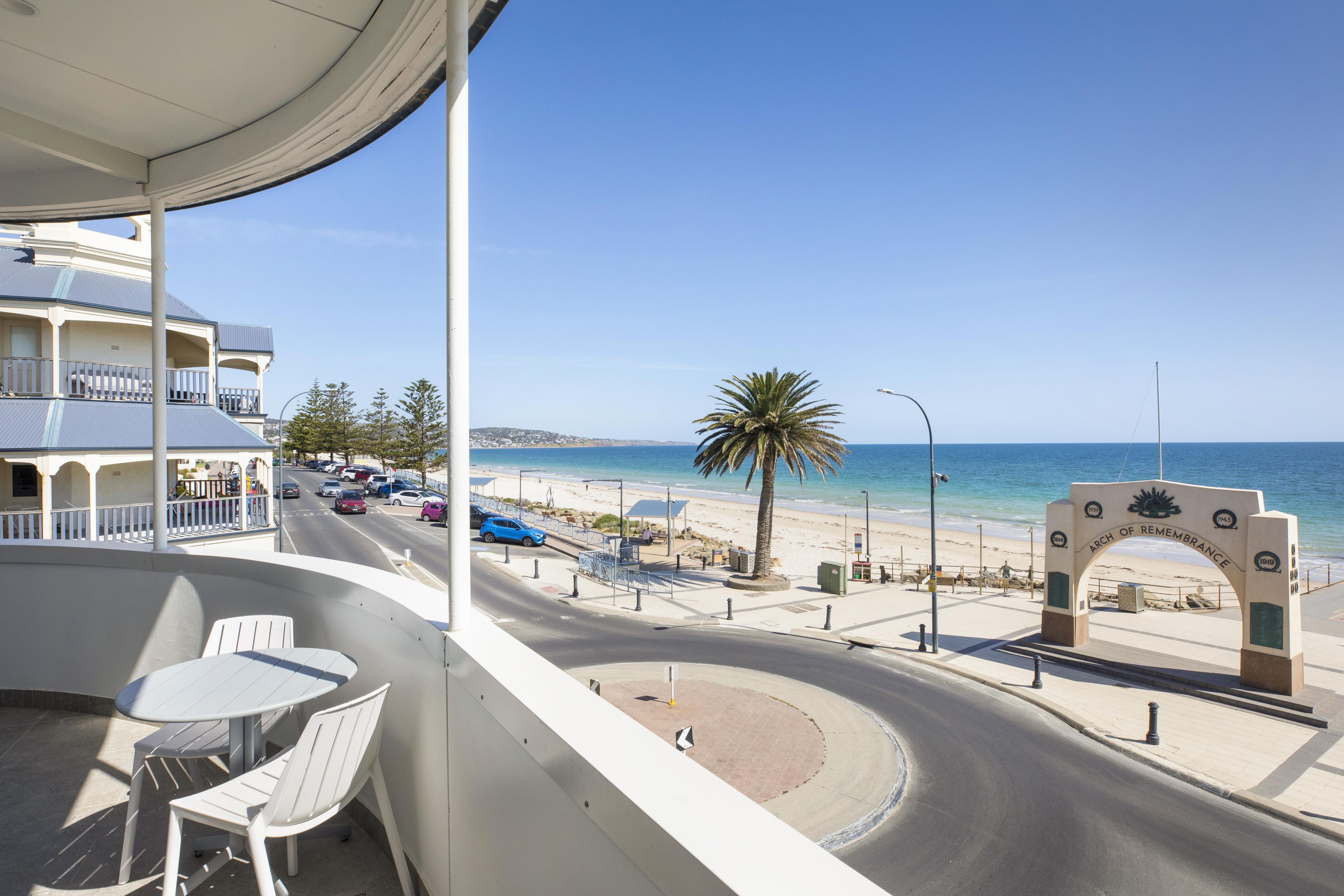 Un balcón con vista a una playa, una palmera y una carretera con coches.