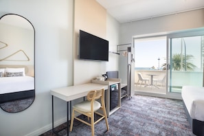 A hotel room with a bed, a desk, a chair, a TV, and a balcony with a view. - Nightcap at Esplanade Hotel (Brighton)