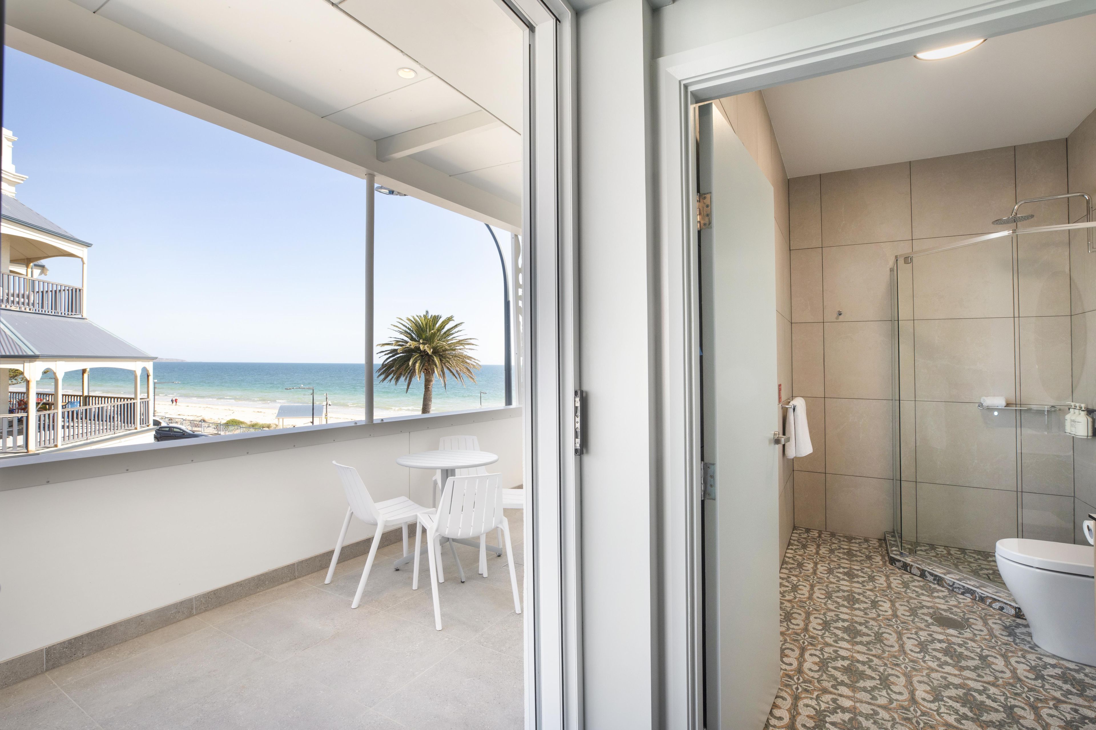 A balcony with a view of the beach, a glass-enclosed shower, and a small table with chairs.