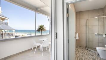 A balcony with a view of the beach, a glass-enclosed shower, and a small table with chairs.