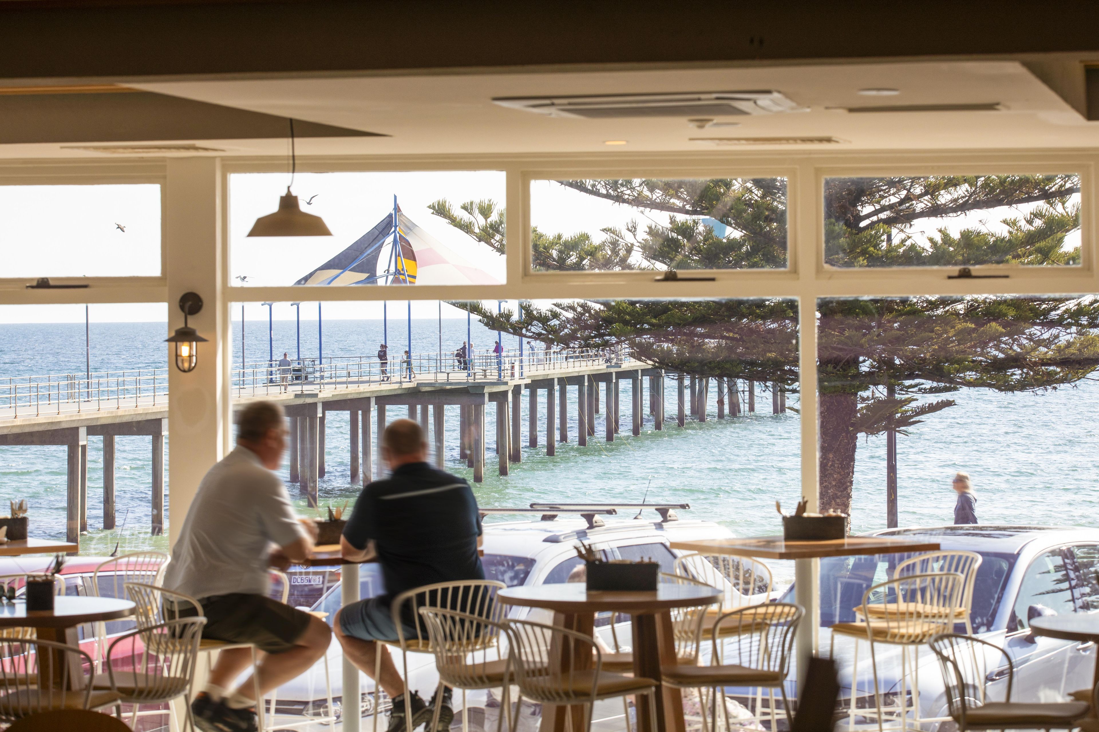 En restaurang med stora fönster som vetter mot en brygga och havet.