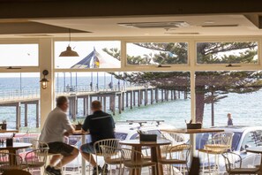 Un restaurante con grandes ventanales que dan a un muelle y al mar.