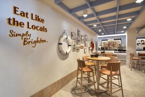 A restaurant interior with a wall sign reading 'Eat Like the Locals Simply Brighton.' There are tables and chairs, a bar area in the background, and framed pictures on the wall. - Nightcap at Esplanade Hotel (Brighton)