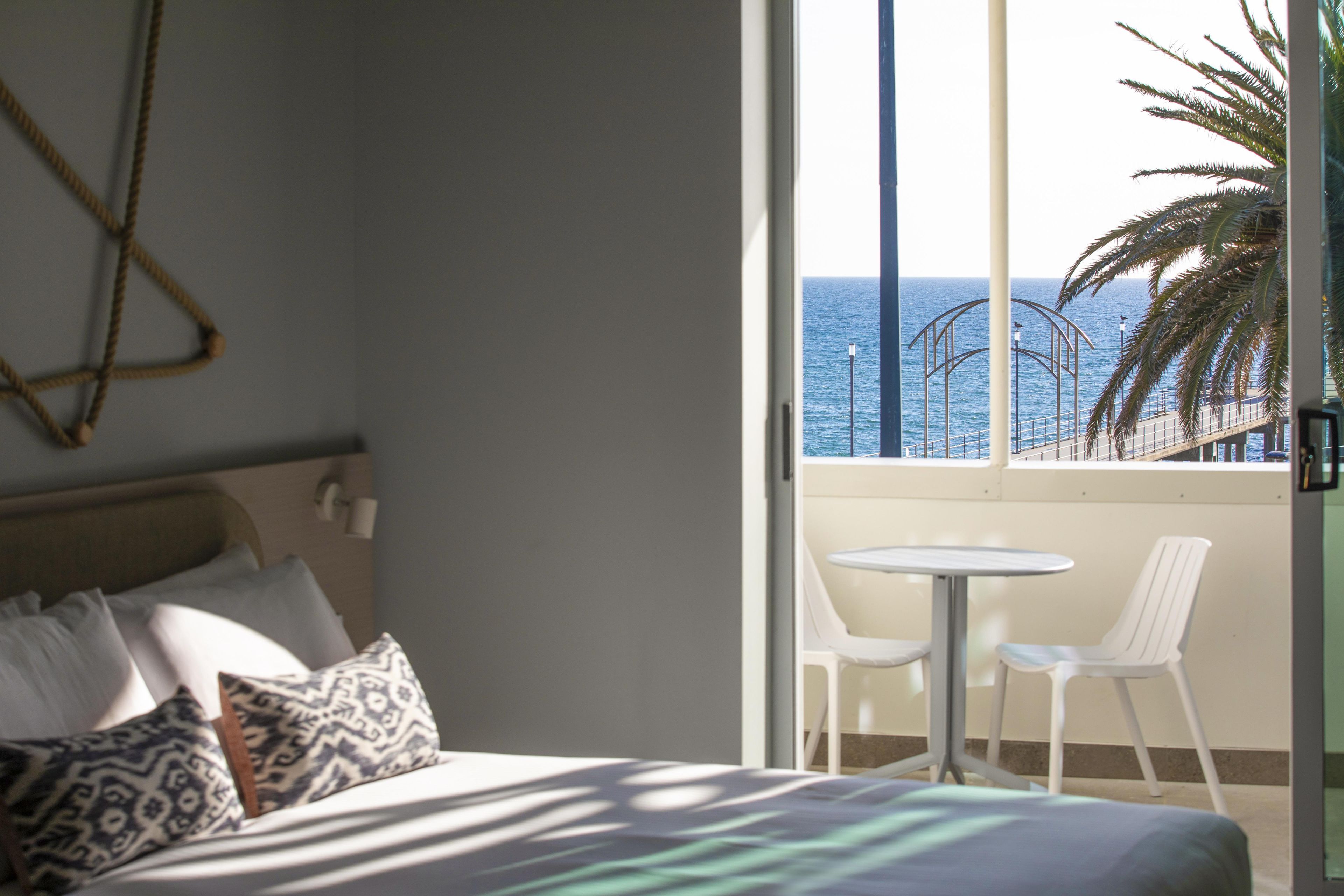 Habitación de hotel con una cama, un balcón pequeño con mesa y sillas, y vista al mar.