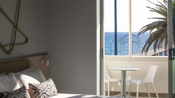 Habitación de hotel con una cama, un balcón pequeño con mesa y sillas, y vista al mar.