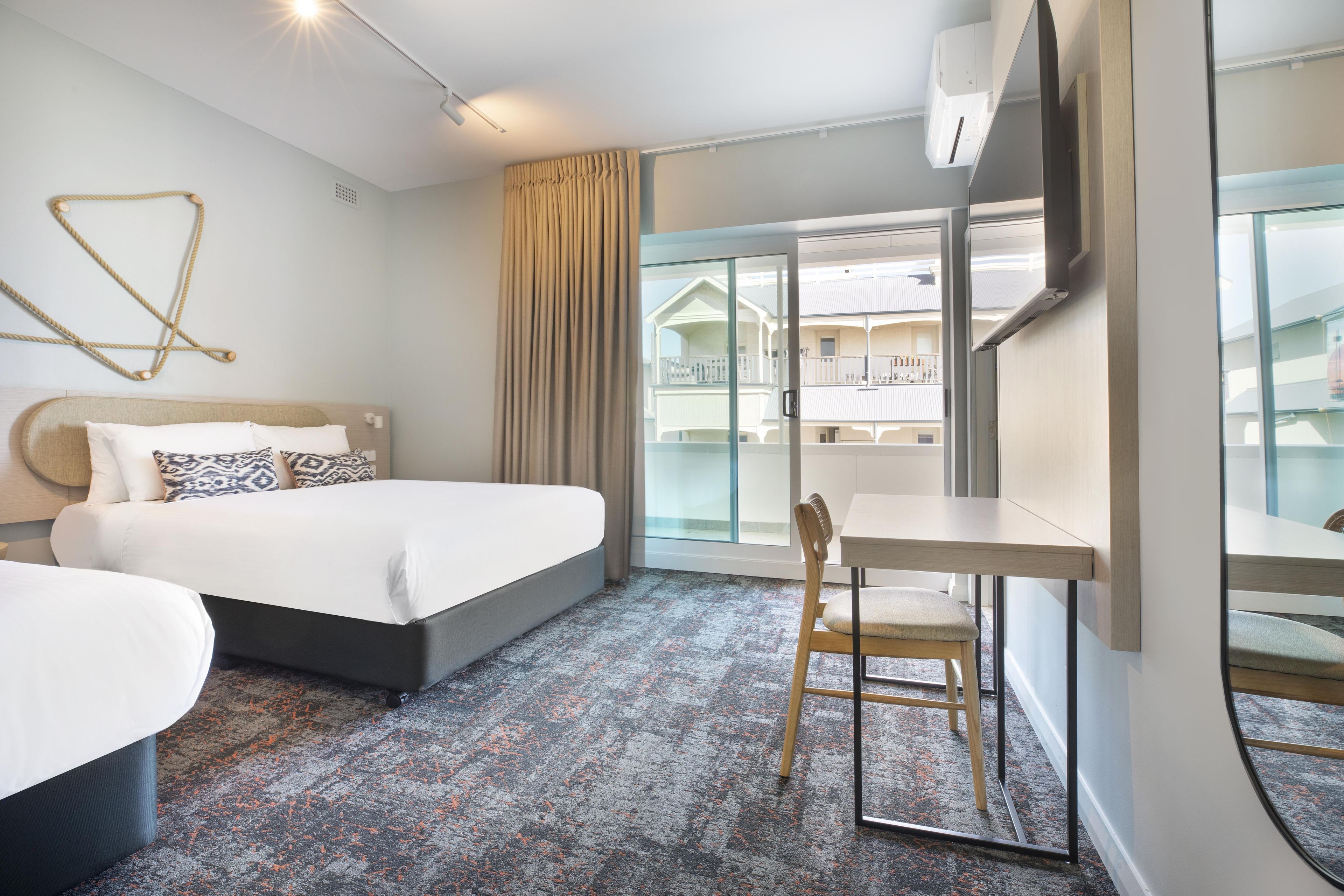 A hotel room with a bed, a desk, a chair, and a view of a building through a glass door.