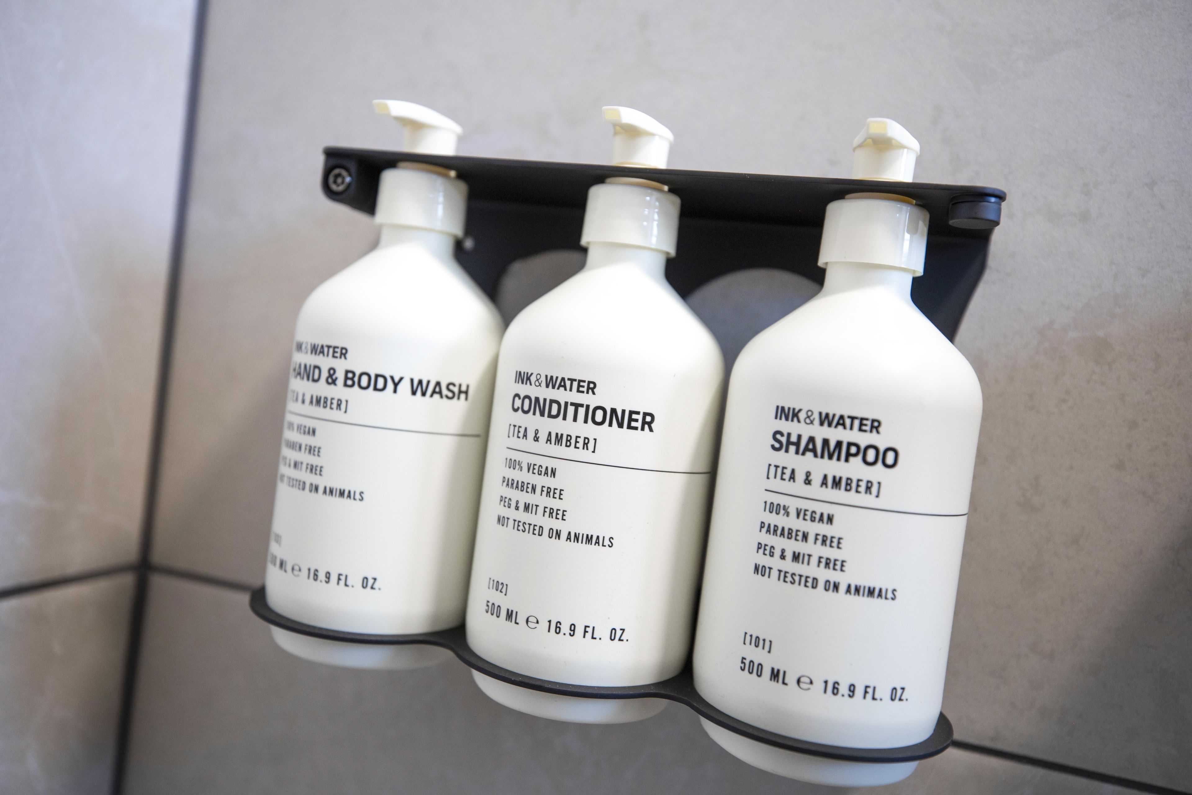 Trois bouteilles de shampoing, d’après-shampoing et de gel pour les mains et le corps, posées sur une étagère noire.
