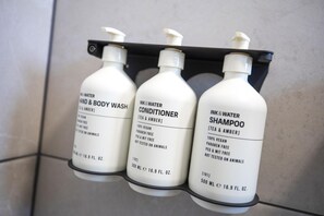 Three bottles of shampoo, conditioner, and hand & body wash on a black shelf. - Nightcap at Esplanade Hotel (Brighton)