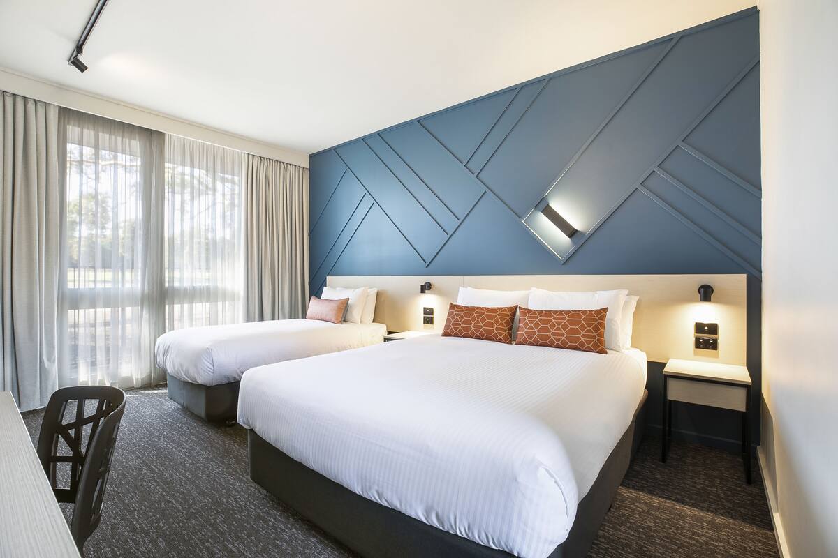 Hotellihuone, jossa on kaksi sänkyä, työpöytä ja tuoli.