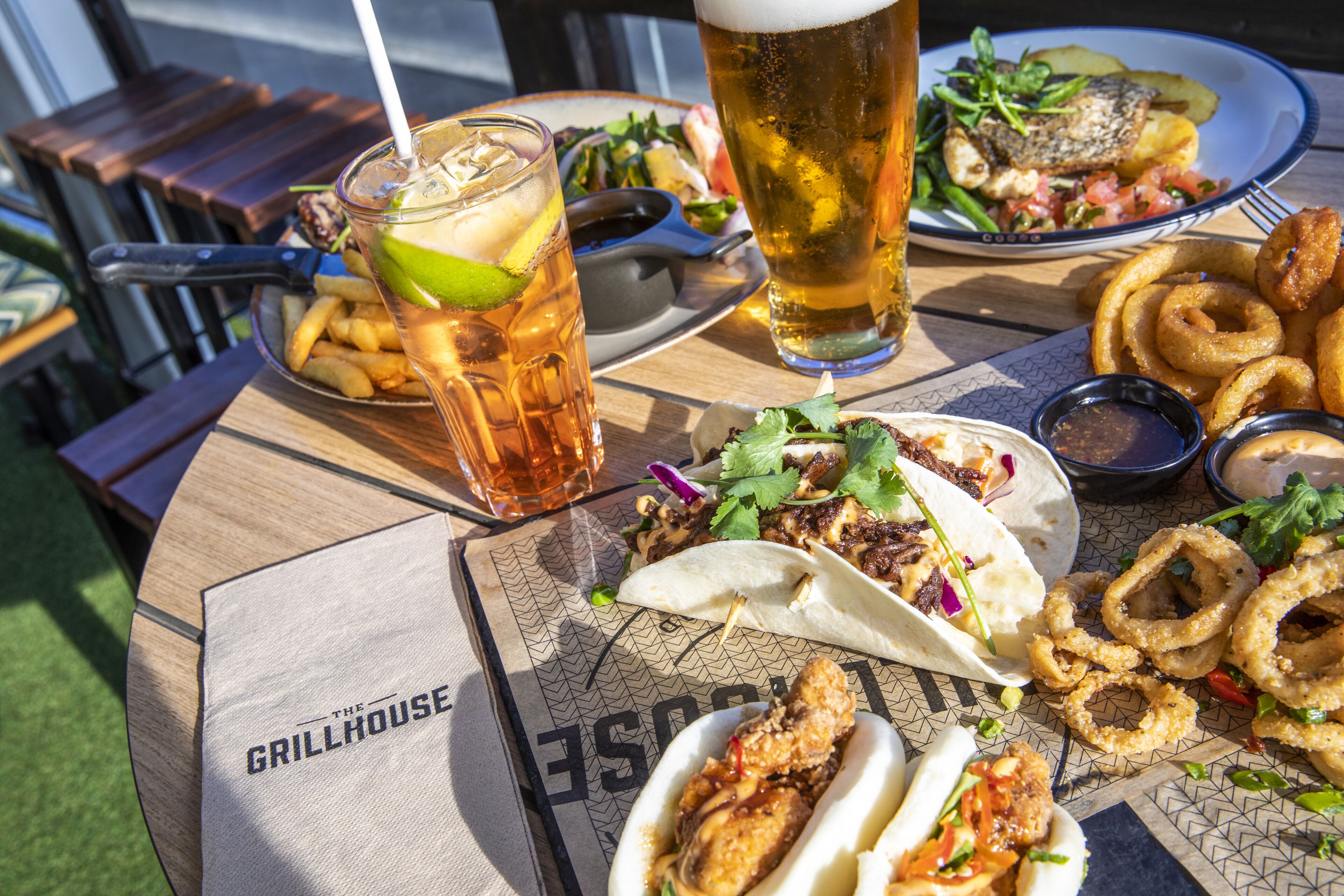 A table with food and drinks, including tacos, onion rings, and a beer.