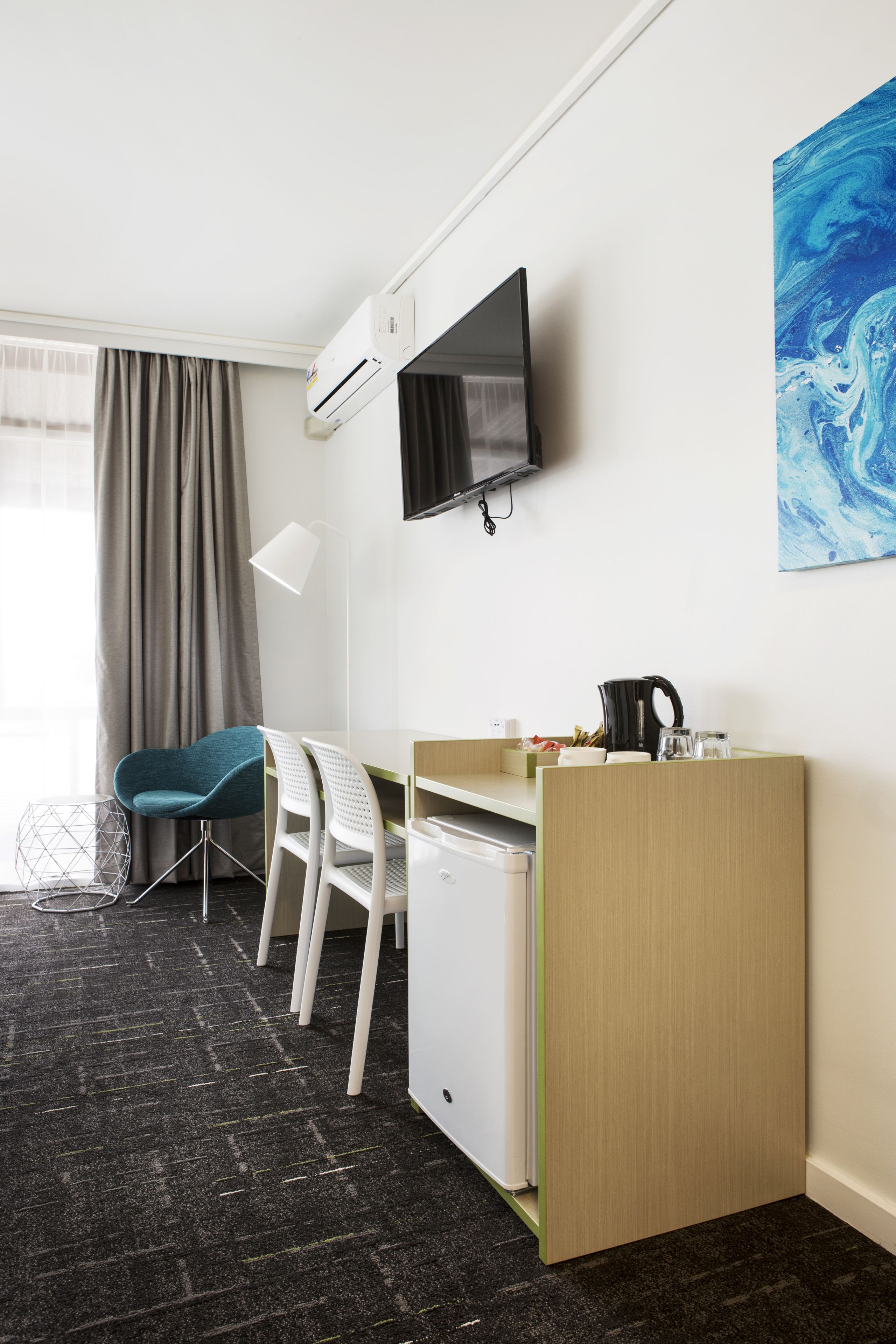 A hotel room with a desk, chair, TV, and artwork on the wall.