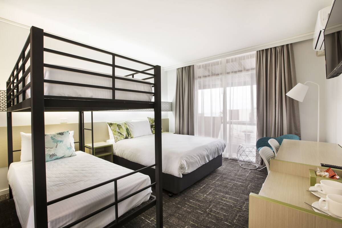 A hotel room with two bunk beds, a desk with a chair, a TV, and a window with curtains.