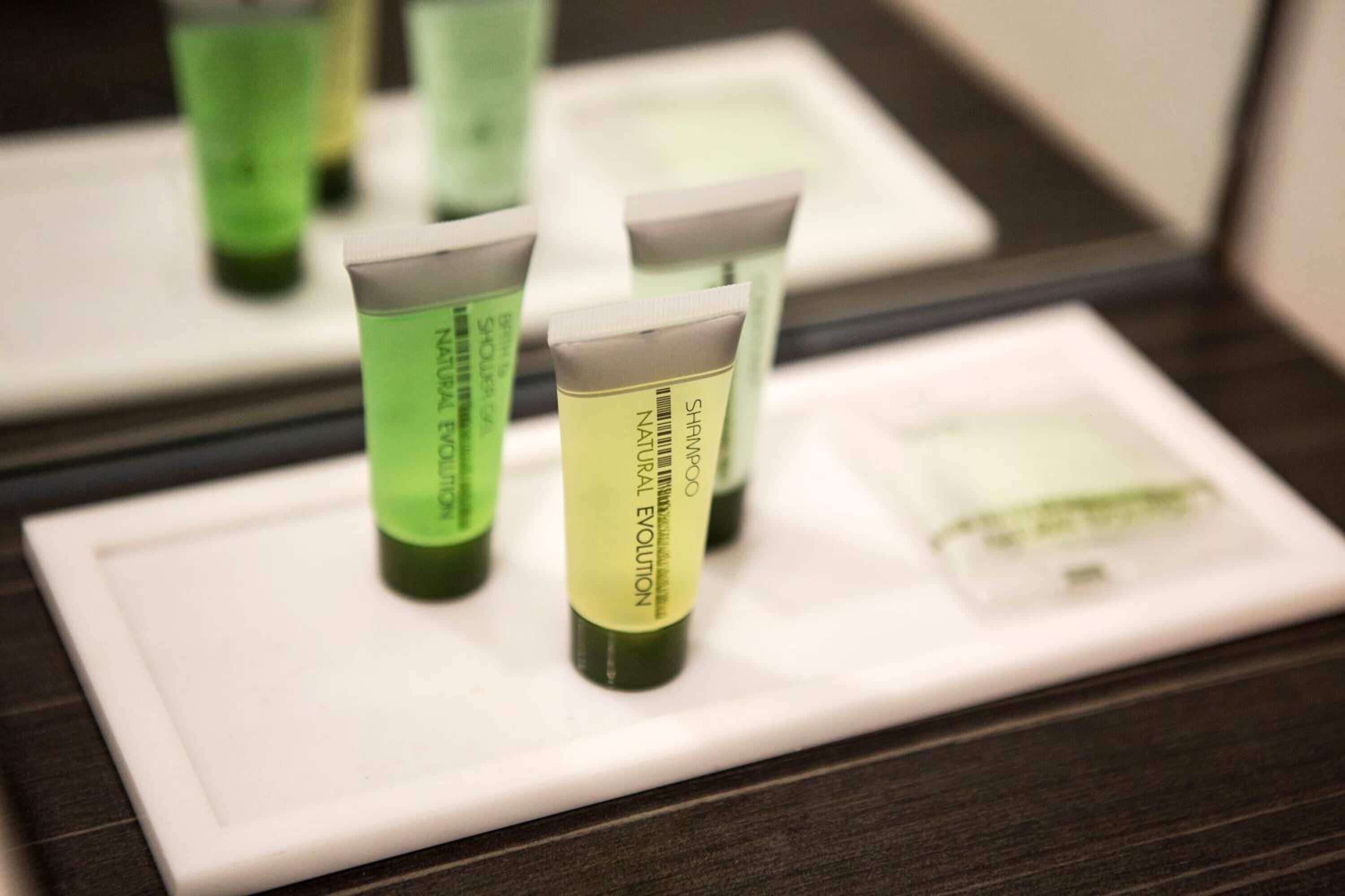 A bathroom with a mirror reflecting three green bottles of shampoo and a white tray.