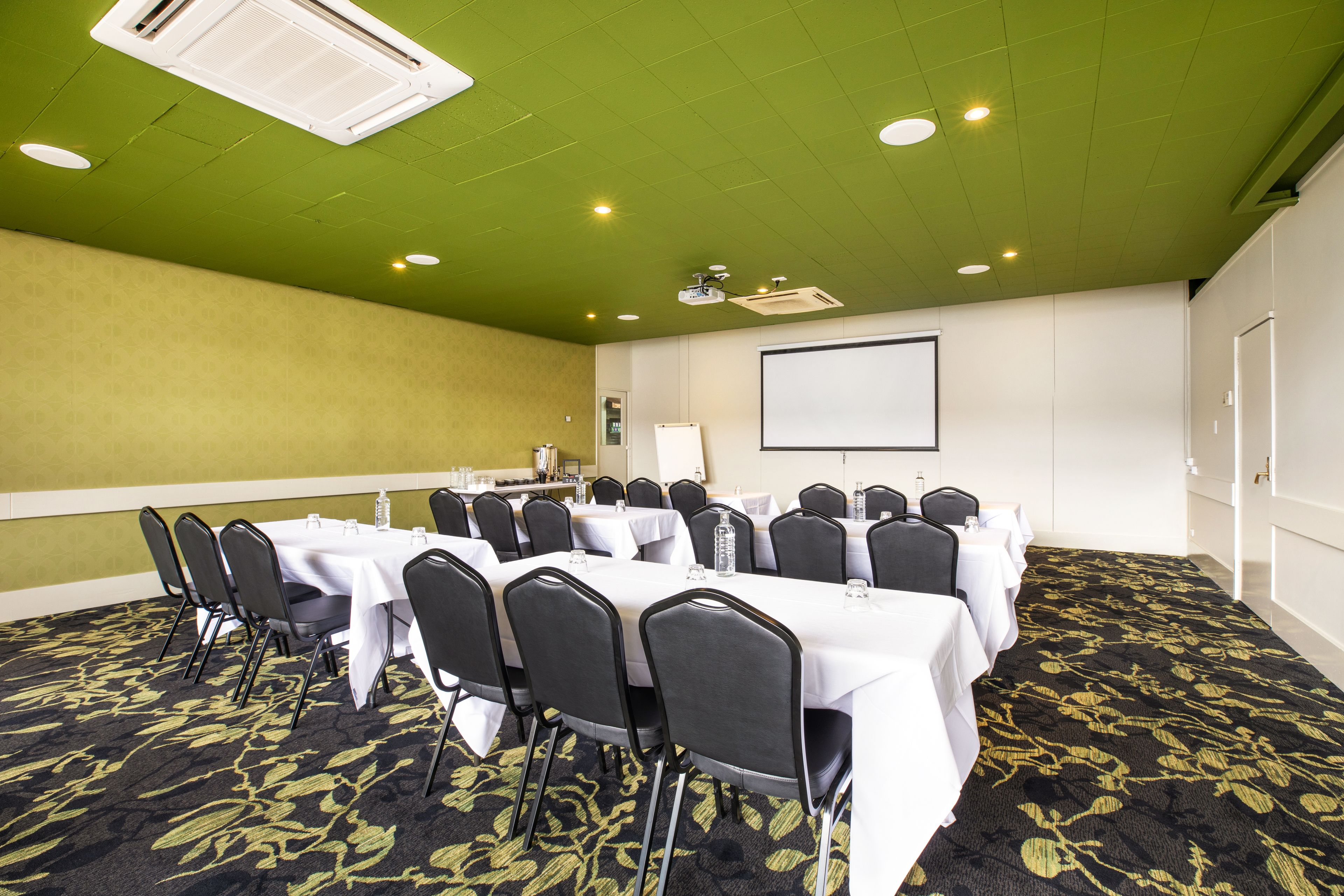 A conference room with tables, chairs, a projector screen, and a carpeted floor.