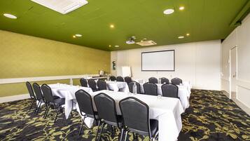 A conference room with tables, chairs, a projector screen, and a carpeted floor.