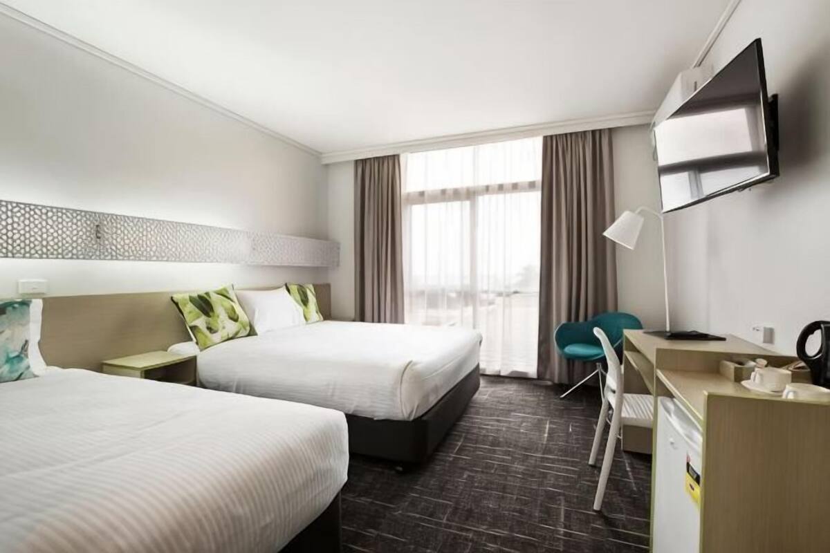 A hotel room with two beds, a desk, a chair, a TV, and a window with curtains.