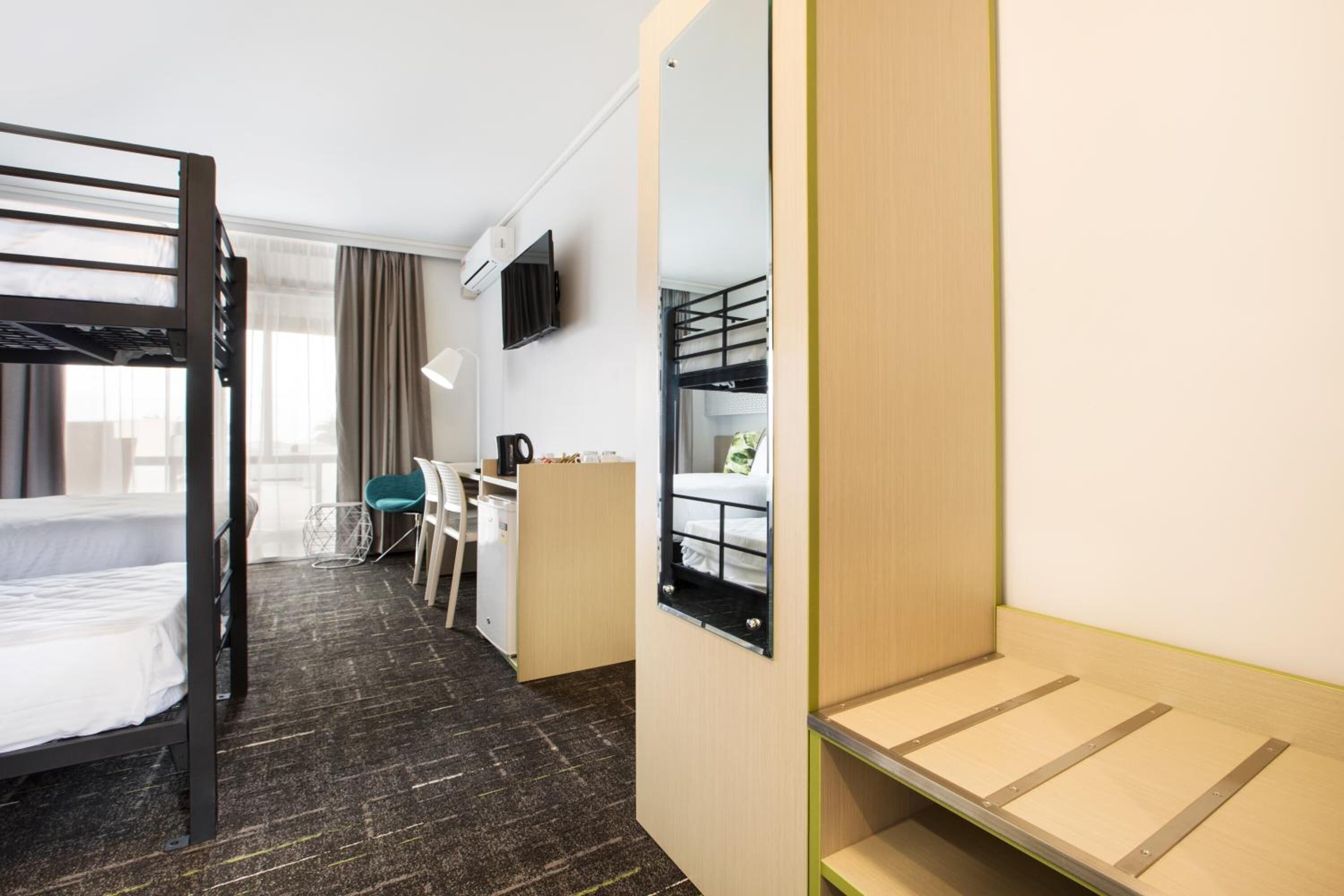 Een hotelkamer met stapelbedden, een bureau, een stoel, een spiegel en een raam met gordijnen.