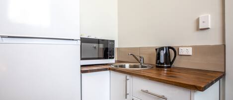 A compact kitchen with a white refrigerator, a microwave, a sink, and a coffee maker.