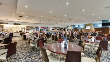 A spacious restaurant with multiple dining tables and chairs, a counter for ordering, and a television screen on the wall.
