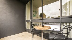 A balcony with a round table and two chairs, a glass door, and a view of the outside.