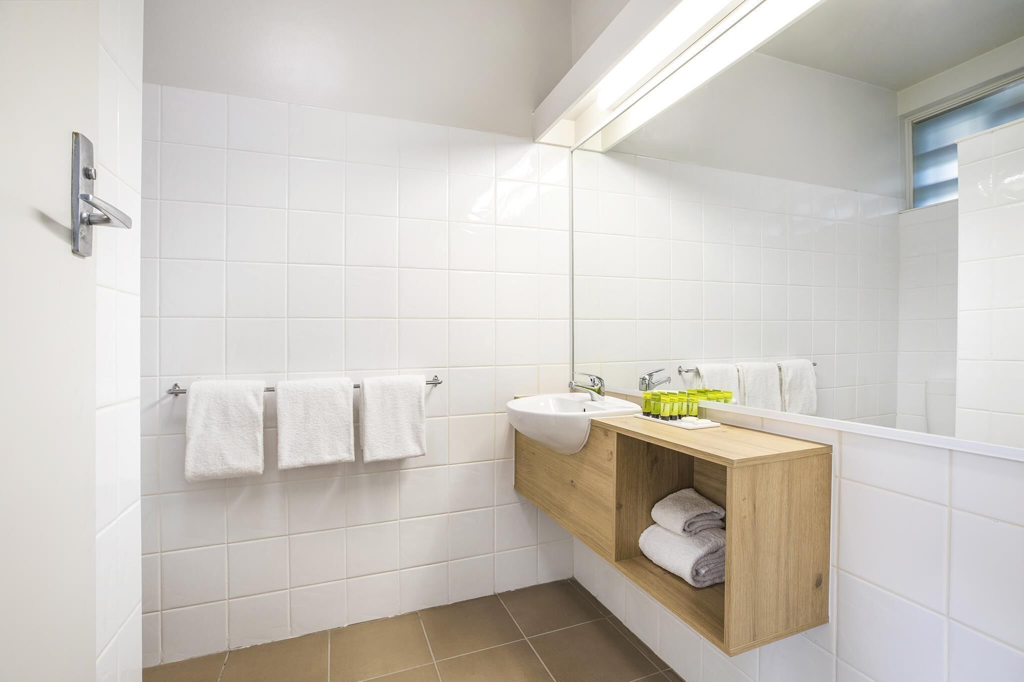 A modern bathroom with white tiles, a wooden vanity, a sink, and a mirror.