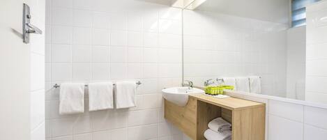 A modern bathroom with white tiles, a wooden vanity, a sink, and a mirror.