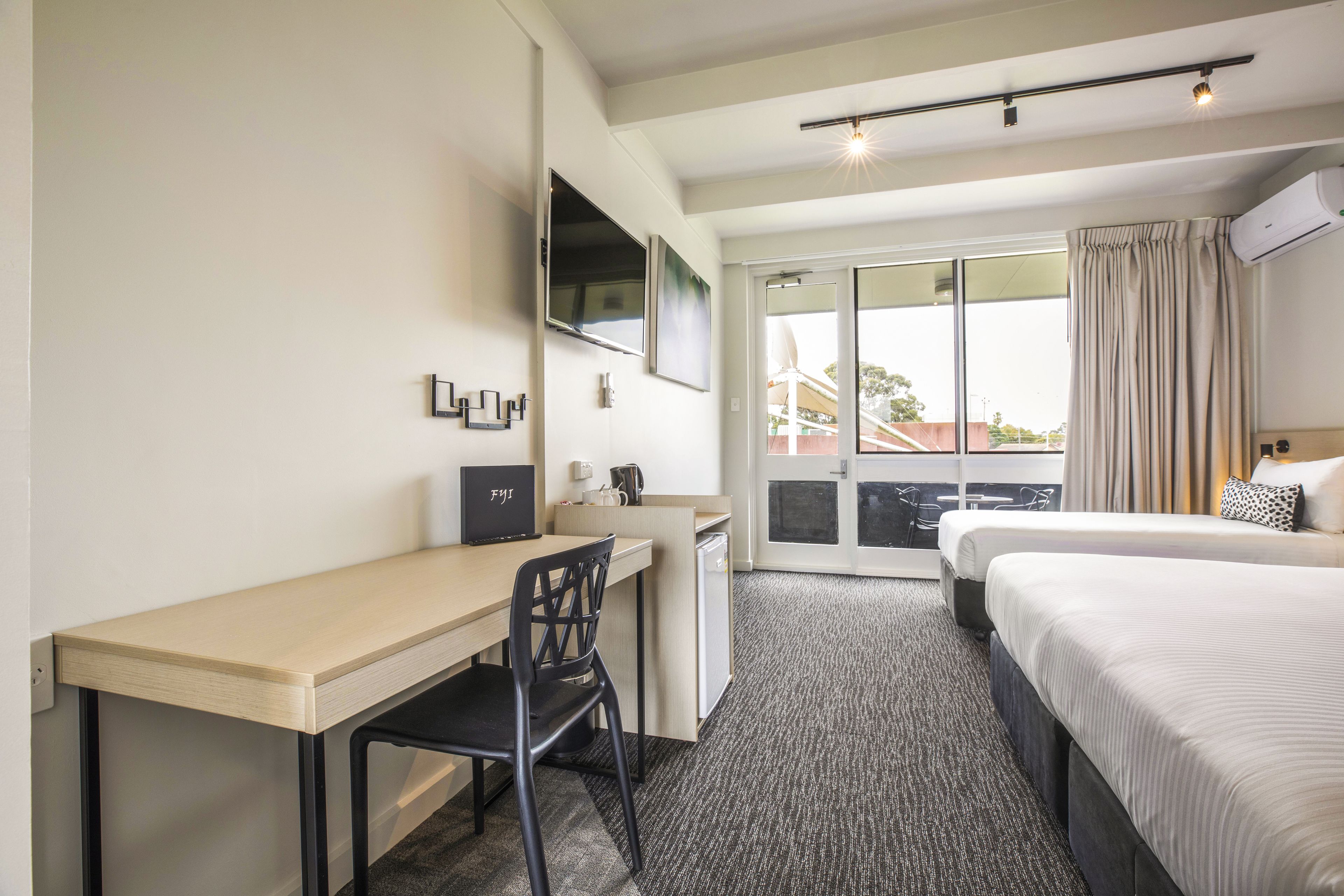Habitación de hotel con escritorio, silla, dos camas, televisión y balcón con cortinas.