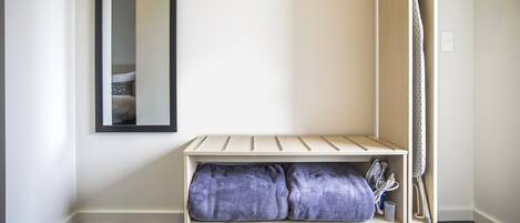 A corner of a room with a bench, a mirror, and a hanging garment.